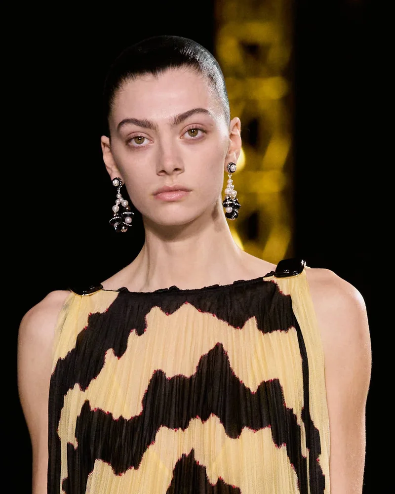 Модель Chanel осінь-зима 2026/27 з коротким волоссям, гладко зачесаним назад, і великими сережками